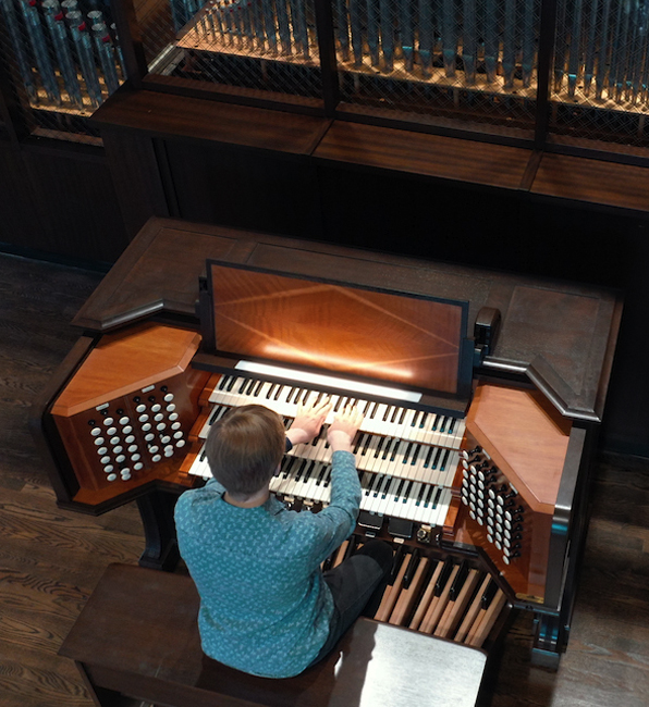 Person playing a large pipe organ with multiple keyboards, pedalboard, and stops